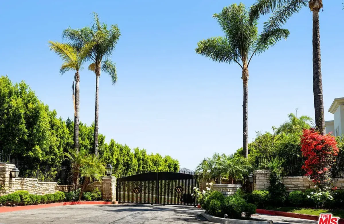 a gated driveway with palm trees and a blue sky