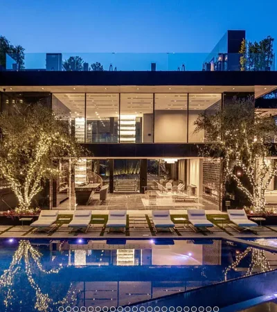 a pool with lights and chairs in front of a house