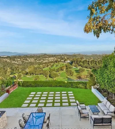 a patio with a table and chairs on a lawn with trees and a valley in the background